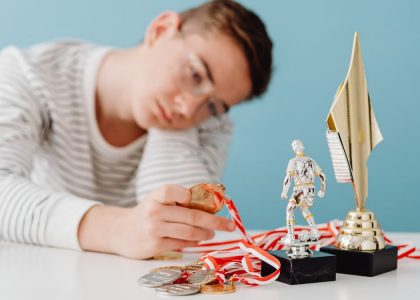 A thoughtful teenager sits by a table with various trophies and medals.
